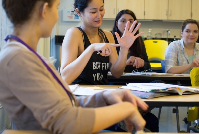 A woman in an occupational therapy classroom points to her hand to illustrate an exercise.