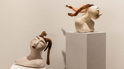 Two ceramic buffs facing in opposing directions, with braided hair floating from each head
