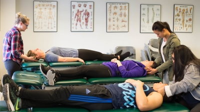 Physical therapy students laying on green tables with other students standing by their heads