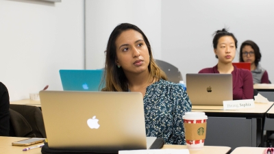 Students in class listening to a lecture with their laptops open.
