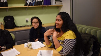 An MA student speaking while seated at a conference room table.