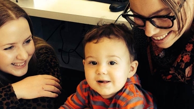 A child sitting on a speech-language pathologist's lap with another woman squatting next to the child.
