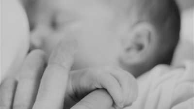 A tilt-shift photo of a breastfeeding child holding onto their mother's finger