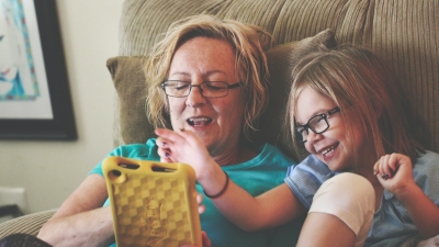 A woman and a young girl sit on a couch together and learn on a tablet