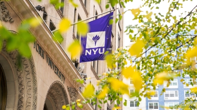 NYU flag on building with fall foliage in the foreground