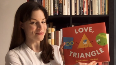 Dr. Moira Dillon holding up a book called "Love, Triangle" to read