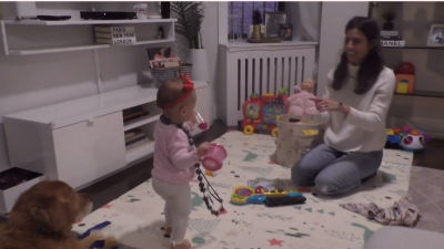 An infant and a woman playing on a rug while a dog lays nearby