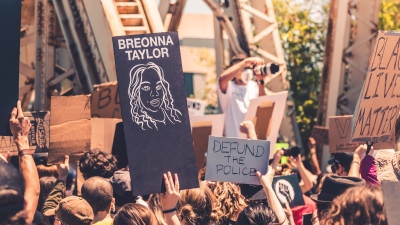 A photo of a Black Lives Matter protest from summer of 2020 featuring protestors holding signs that say "Black Lives Matter," "Breonna Taylor," and "Defund the Police"