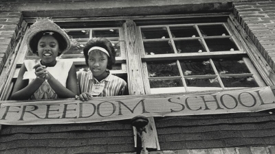 Two young black girls smile and lean out of the window of a freedom school
