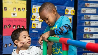 Preschool students build a structure from plastic interlocking tubes. 