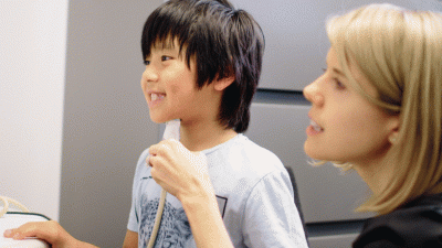 Dr. Tara McAllister holding a biofeedback device under the chin of a young boy.