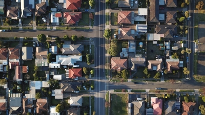 A top down photo of a suburban neighborhood where only the roofs are visible, along with occasional cars and trees