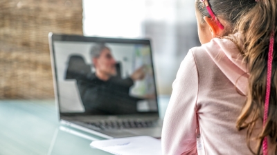 A photo of a young girl in a pink sweatshirt looking at a laptop with an out of focus image of a man on the screen