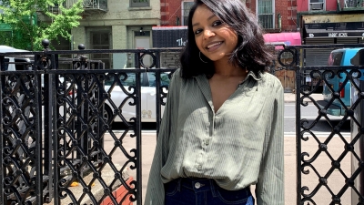 woman smiling on front of gate and buildings