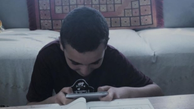 A photo of a child in front of an academic workbook holding a handheld video game controller