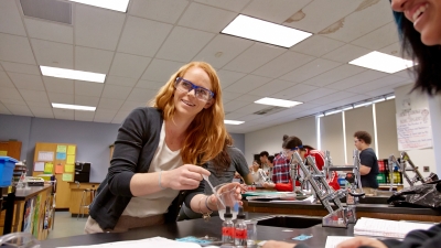 Smiling female science teacher uses a dropper to deposit liquid into a beaker