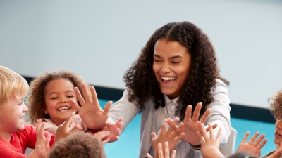 School children gather in a circle to give their teacher a high five.
