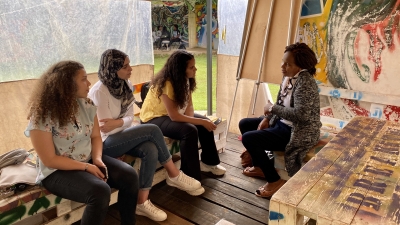 Four people sit inside a large tent, talking.
