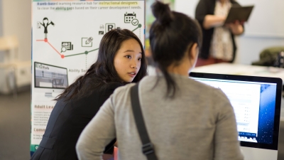 student demonstrating their work in front of a research poster and computer