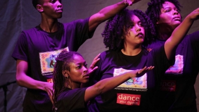 Dark-skinned dancers pose with their arms outstretched, faces serious.