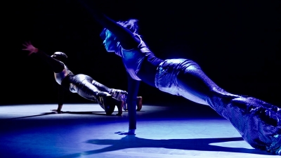 Two dancers in metallic clothing in a stretch pose
