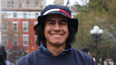 Photo of Ben in Washington Square Park; smiling, wearing a hat and navy blue sweater