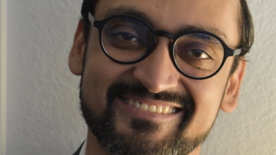 Professional headshot of Haider Fancy; smiling, wearing glasses and collared shirt 