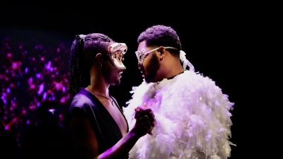 Two performers dressed with masks and a feathery costume doing a slow dance on stage