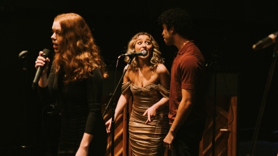 Three singers on stage performing with piano in background