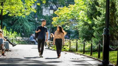 2 students walking in Washington Square Park, trees and greenery in the background