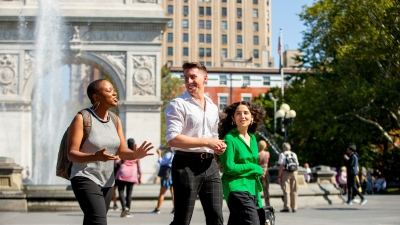 2 female and 1 male student walking, Washington Square Park Arch and fountain in the background