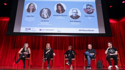 Five panelists on stage with large screen overhead indicating who is who