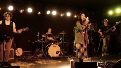 Four students performing on stage, a lead singer, drummer and two guitar players