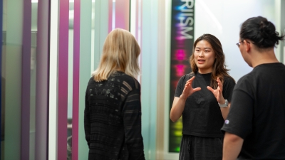 student standing, talking with two faculty members in front of a PRIISM sign