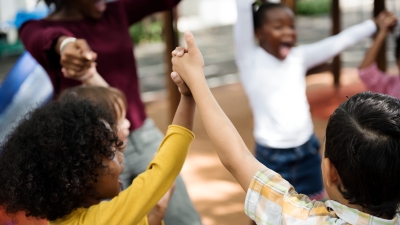 Diverse group of students standing in a circle holding hands up in the air.