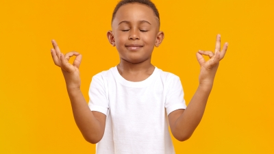 Young black boy meditating in front of a yellow background.
