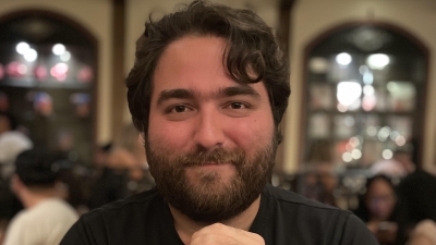 Photo of Marc with his elbows on table, hands clasp in front of him, soft smiling at camera