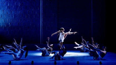 A central dancer in the spotlight with other dancers on the ground around her