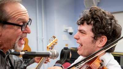 Teacher and student singing and laughing playing guitar and violin