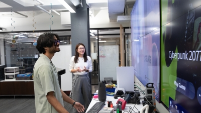 Two students smiling as they look at a wall-mounted screen.  
