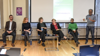Five people sit together for a panel. One man stands and moderates.