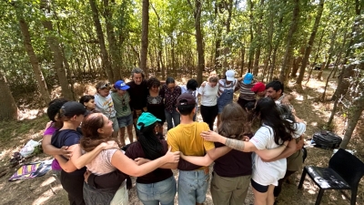 A group of students stands in a circle in the forest, hugging each other