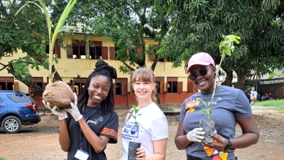 Three women smile at the camera, each one holding a small plant