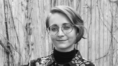 Christina Wusinich in black and white, smiling with glasses. 