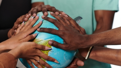 A group of students' hands are placed around a globe.