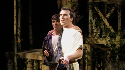 Two actors in costume on stage singing arm in arm