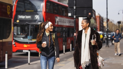 Two students walking in London with a red double decker bus behind them.