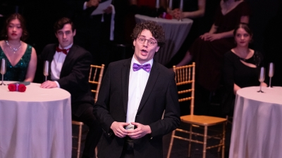 Opera singer on stage wearing a tuxedo and purple bow tie singing solo.