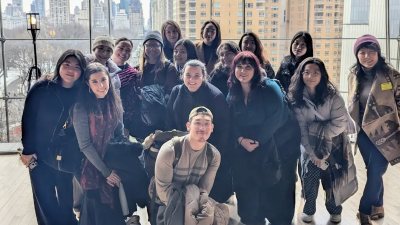 Large group of students standing in front of tall windows posing for the camera