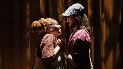 Two actors standing close holding hands and looking into each others eyes lovingly